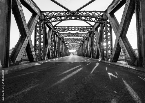 Black and white asphalt road under the steel construction of a bridge in the city on a sunny day. Evening urban scene with the sunbeam in the tunnel. City life, transport and traffic concept. © sergiymolchenko