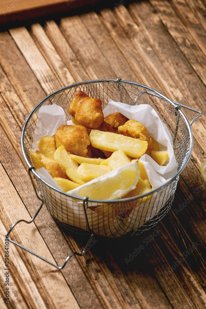 Classic british fast food fish and chips served in frying basket with lemons over wooden plank table. Classic british fast food fish and chips served in frying basket with lemons over wooden plank table.