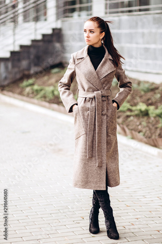 Portrait of a full-length girl on the street in autumn. Young adult girl in an elegant coat outdoors. Promotional coat. Young fashionable brunette woman in a stylish woolen autumn and spring coat.