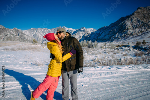 Young loving happy couple embraces and enjoys a new year vacation in the mountains. Guy and girl holding hands on the background of snow-capped mountains. Christmas holidays and travel.
