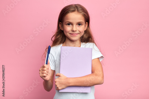 girl holding a book , pen. Back to school concept.isolated pink background, studio shot. lifestyle, free time, kid is ready to study.