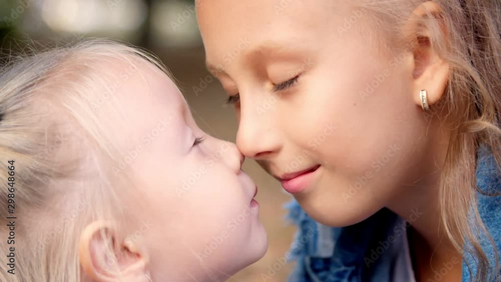 portrait, two little girls sisters , a teenage girl and a little one are huging, rubbing gently their small noses with each other. portrait, two little girls sisters , a teenage girl and a little one are huging, rubbing gently their small noses with each other.