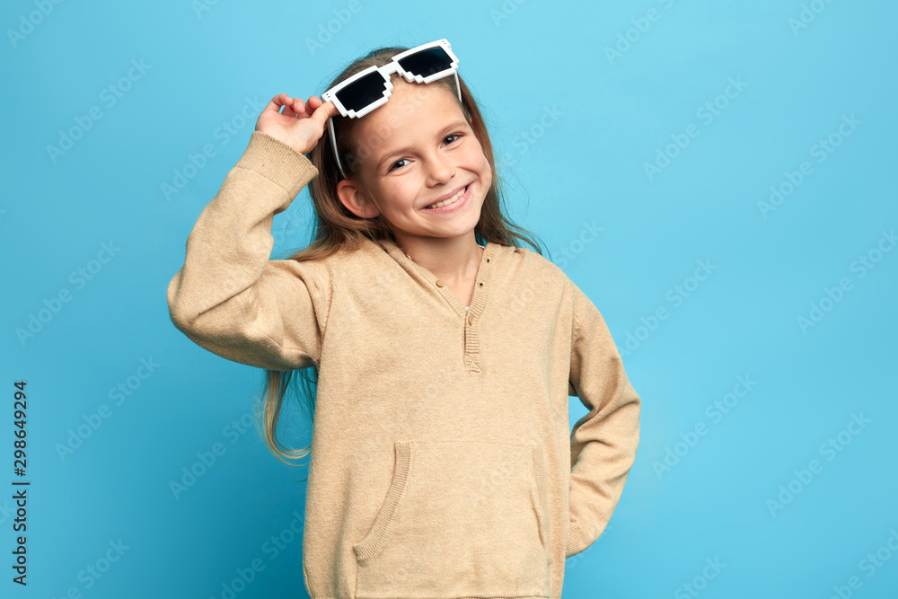 positive charming girl with sunglasses on her head posing to the camera. close up portrait, isolated blue background, studio shot, lifestyle, free time, spare time.