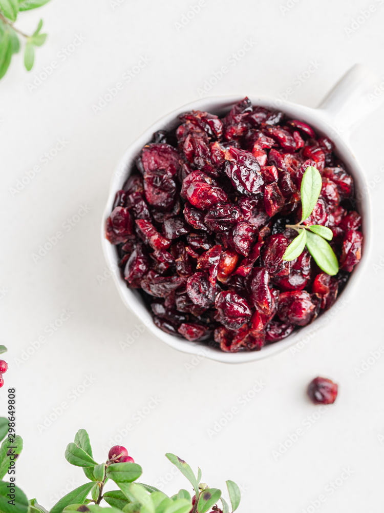 Dried cranberries with green leaves and fresh berries in white bowl white background Dried cranberries with green leaves and fresh berries in white bowl white background