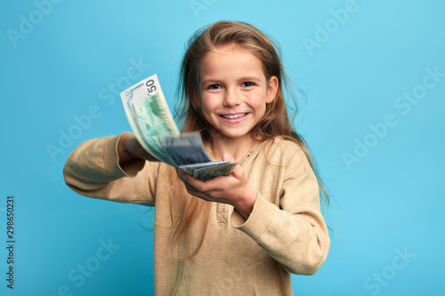 rich girl concept. smiling cheerful girl donets money on stray animals. close up portrait, isolated blue background, studio shot.luxiry life, spender, teaching children to manage with money photo