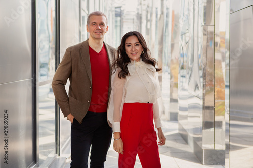 Fashion style Clothes  business casual. Respectable Businessman Wearing brown jacket and sweater and Woman in red pants and a stylish white shirt looking at camera and smiling