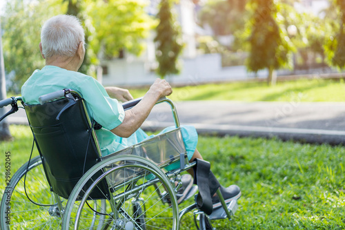 Happy Asian senior man in wheelchair relaxing or resting alone after walking or exercise with caregiver outside at the park. elderly people happy lifestyle.  Patient or Retirement and life concept
