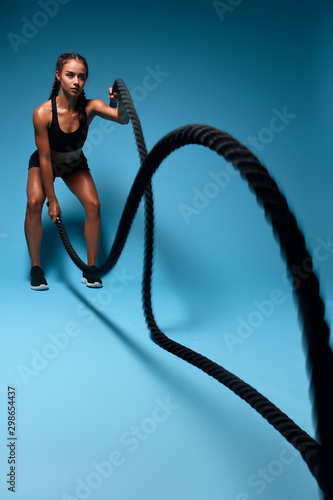 fit slim strong girl working out with battle ropes, full length photo. isolated ble background, studio shot.leisure, body and health care