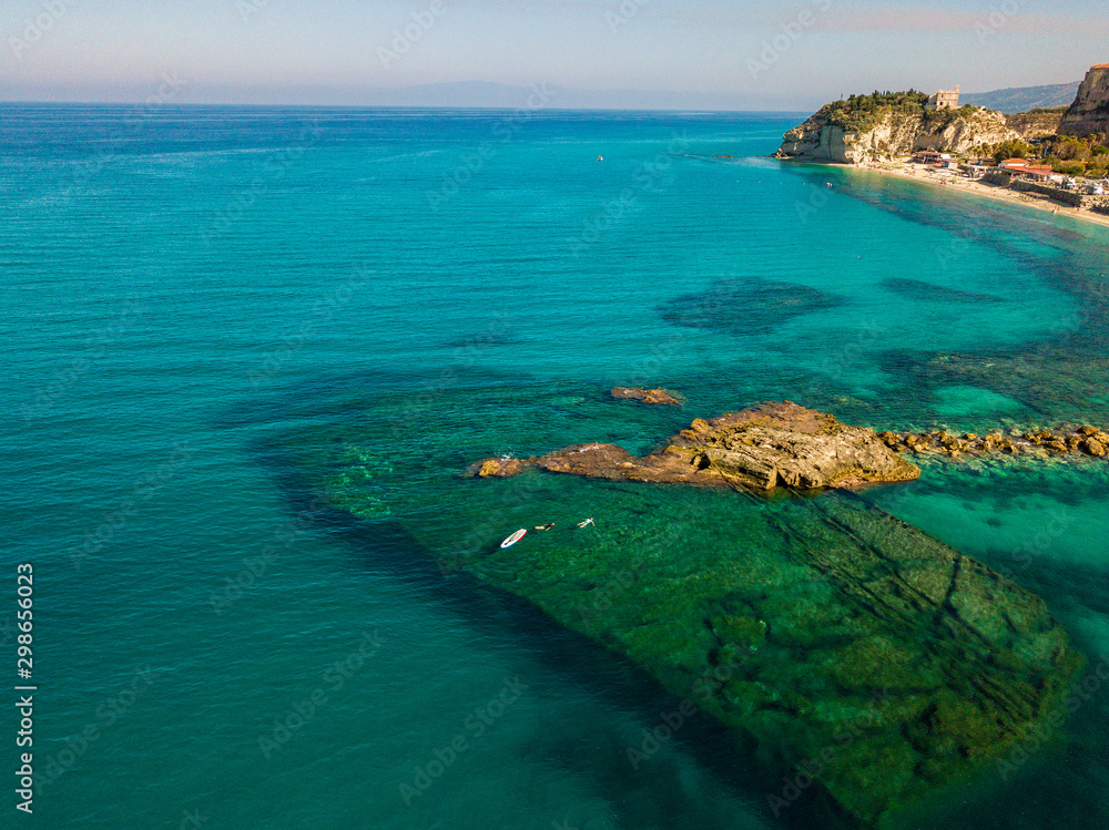 Aerial view of a beach with umbrellas and bathers. Promontory of the Sanctuary of Santa Maria dell'Isola, Tropea, Calabria, Italy.