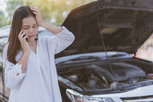 serious young Asian woman using talking smartphone  with Contact an auto mechanic or insurance after Accident or broken down car on street. Maintenance, engine maintenance or car radiators Concept © Joke Phatrapong