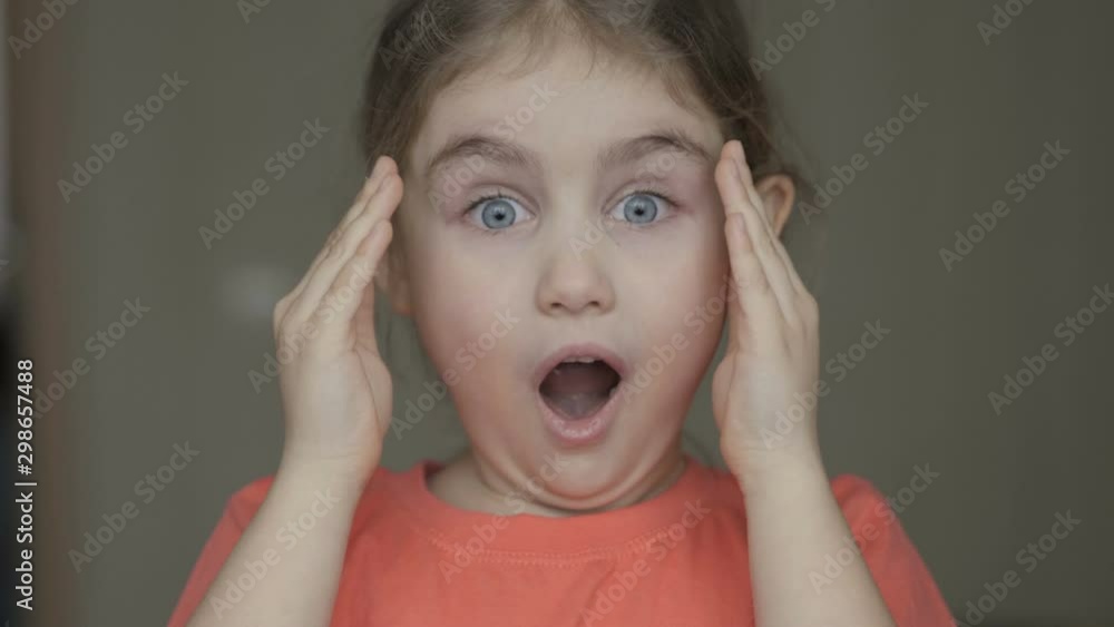 Cute little girl open her face with hands. Girl looks and is surprised and happy to receive a surprise. Portrait little young girl with blue eyes looking at camera. Closeup Cute little girl open her face with hands. Girl looks and is surprised and happy to receive a surprise. Portrait little young girl with blue eyes looking at camera. Closeup