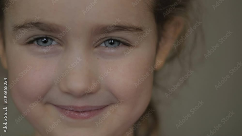 Close up of a little blonde cute girl face. Face portrait closeup. Beautiful child looking at the camera and smiling . Girl blinking her eyes and smiling. Indoors. Close up of a little blonde cute girl face. Face portrait closeup. Beautiful child looking at the camera and smiling . Girl blinking her eyes and smiling. Indoors.