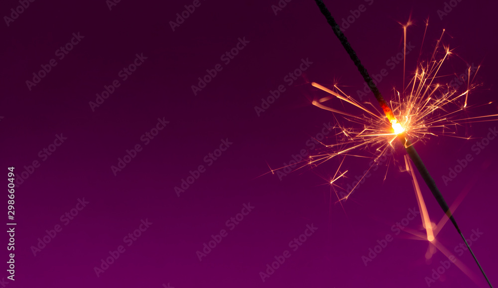 Obraz premium Burning christmas sparkler on purple background with room for text