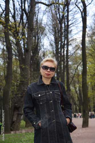 A beautiful woman in dark glasses , against the background of trees, looks at the camera,