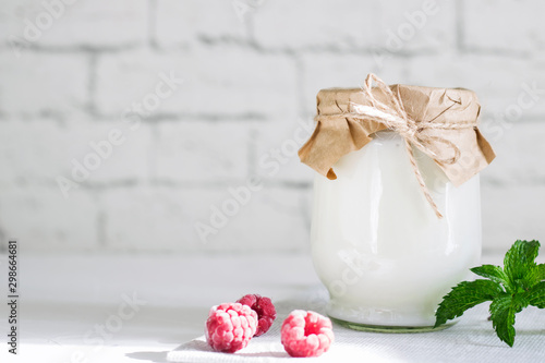 Foto Organic probiotic milk kefir drink or yogurt in glass containers, with raspberry, on the white grey background