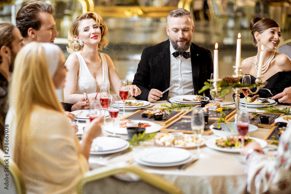 Elegantly dressed people having a festive dinner indoors - obrazy, fototapety, plakaty 