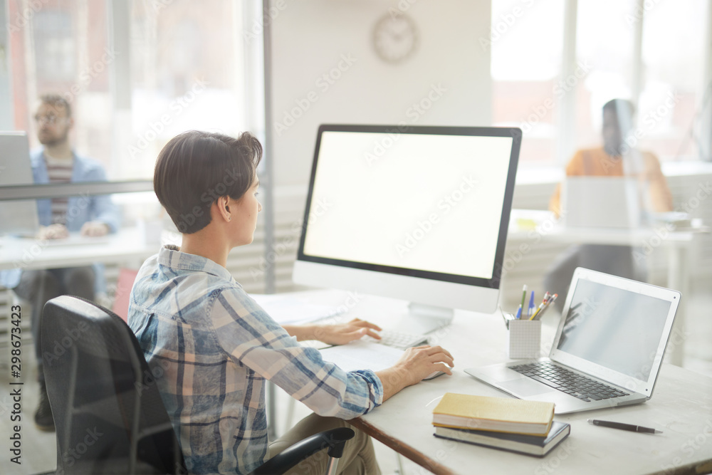 Side view portrait of modern young woman using computer in office, focus on blank white screen, copy space Side view portrait of modern young woman using computer in office, focus on blank white screen, copy space