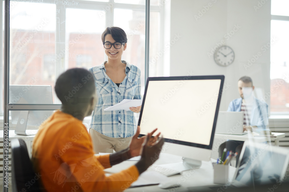 Portrait of smiling young woman handing documents to African-American man while working in office, copy space