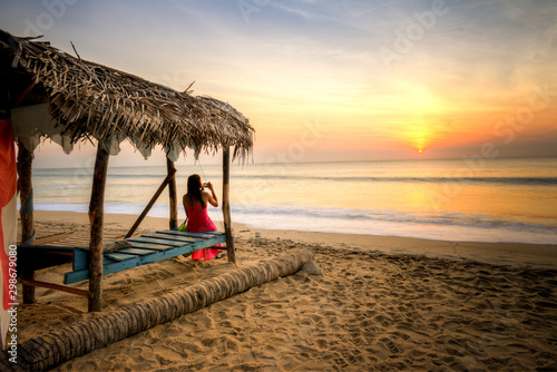 femme en rouge photographie un couché de soleil sur une plage de Arugam Bay au Sri lanka photo