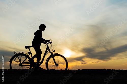 Boy , kid 10 years old riding bike in countryside, silhouette of riding person at sunset in nature