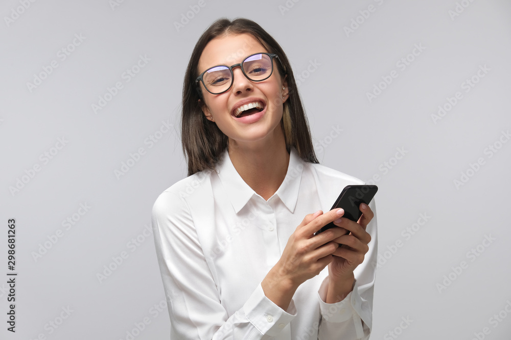 Positive laughing lady in glasses and white T-shirt isolated on background holding smartphone in hands Positive laughing lady in glasses and white T-shirt isolated on background holding smartphone in hands