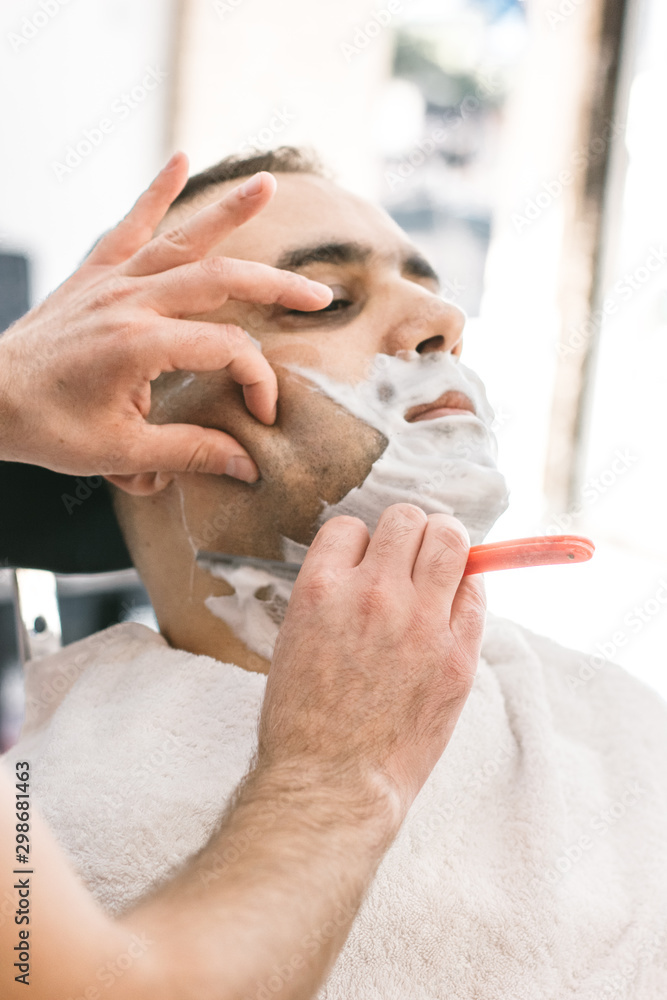 Hairdresser shaves a beard to a man with a razor in the barbershop Hairdresser shaves a beard to a man with a razor in the barbershop