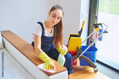 Young attractive cleaner in uniform diligently do her work of cleaning house in morning, wearing yellow protective gloves. Window background