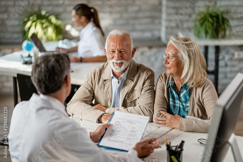 Photos Happy mature couple talking to a doctor while going through their medical reports