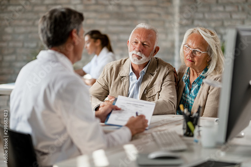 Mature couple planning their health insurance policy with a doctor at clinic. photo