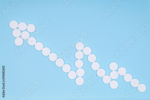 Blue medicine background with arrow of white pills form of success graph.White round pills blue background. Increase dosage medication. Growing up chart with white arrow. Empty place insert text copy