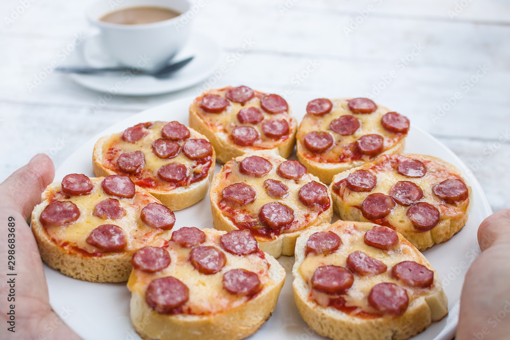 hands holding plate with mini pepperoni pizza snadwiches  close up