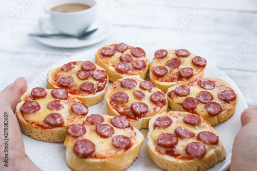 hands holding plate with mini pepperoni pizza snadwiches  close up © Darya