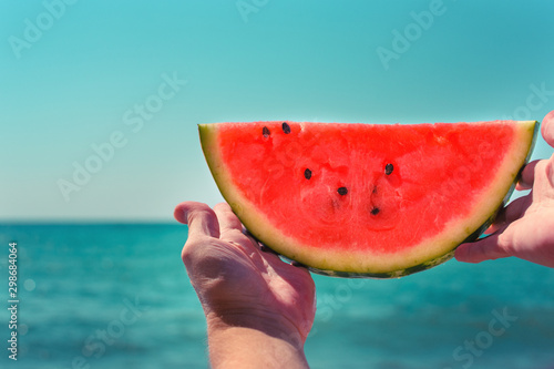 Watermelon, juicy, red slice in the hands of woman against the background of the ocean, in the rays of sunlight. Diet of tropical fruits.