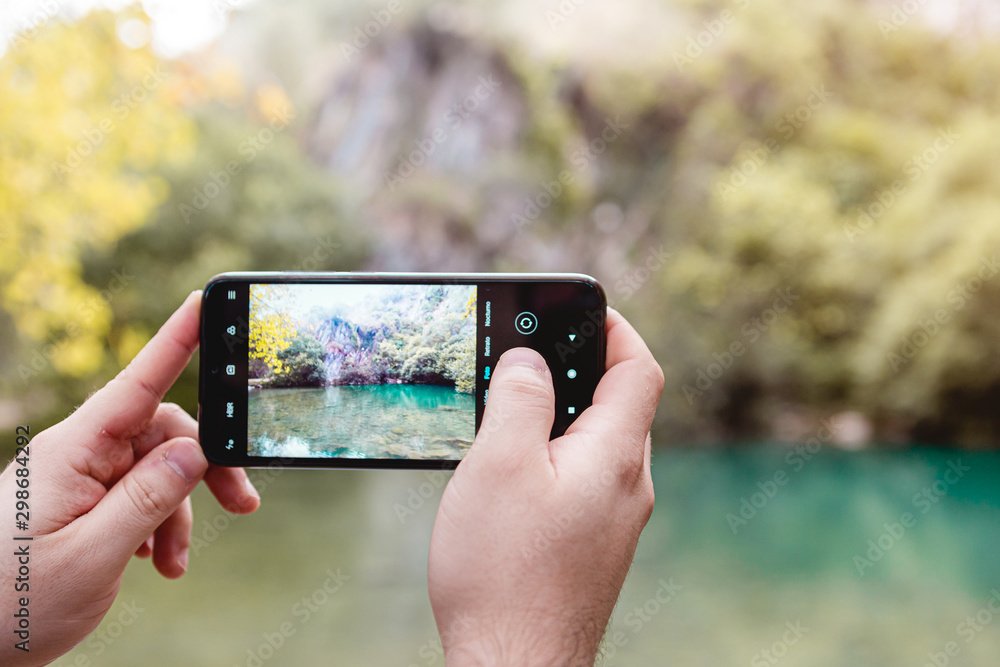 Person hands taking a picture with a mobile phone of the nature at the river