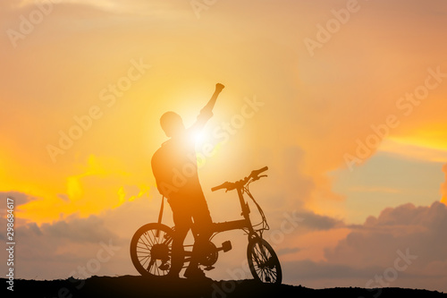 Silhouette of a male sitting on bicycle with a raised hand at sunset