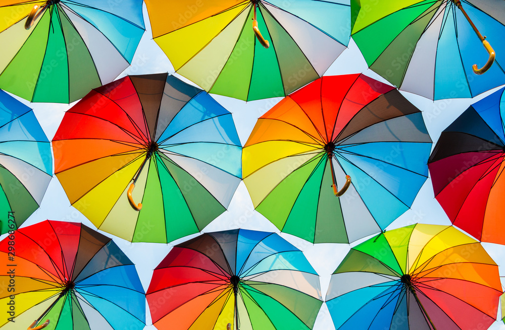 a collection of open umbrellas floating in the air, each umbrella is painted in all colors of the rainbow, photographed from below - obrazy, fototapety, plakaty 