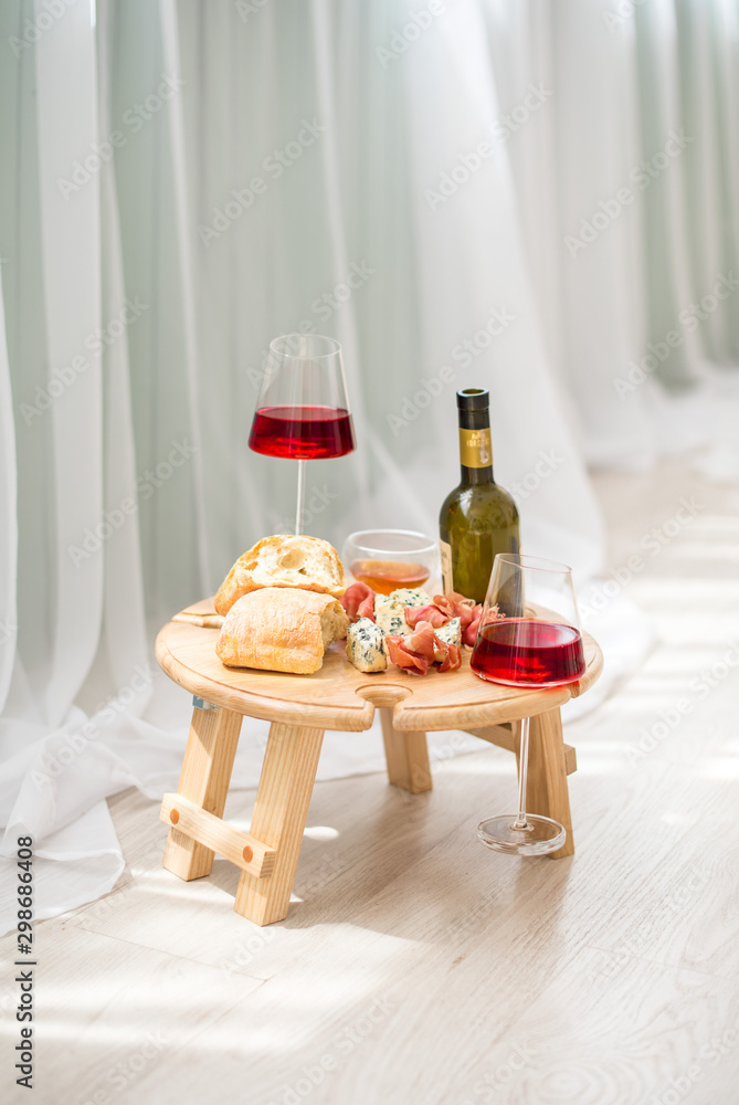 A folding legs tray table is on the bed, red wine in two glasses, blue cheese, camembert, brie, jamon, ciabata, surprise, breakfast in bed, a gift for Valentine's day, birthday, nobody A folding legs tray table is on the bed, red wine in two glasses, blue cheese, camembert, brie, jamon, ciabata, surprise, breakfast in bed, a gift for Valentine's day, birthday, nobody