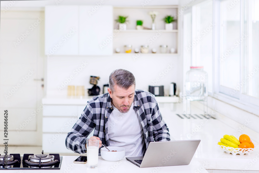 Caucasian man eating cereal while using a laptop Caucasian man eating cereal while using a laptop