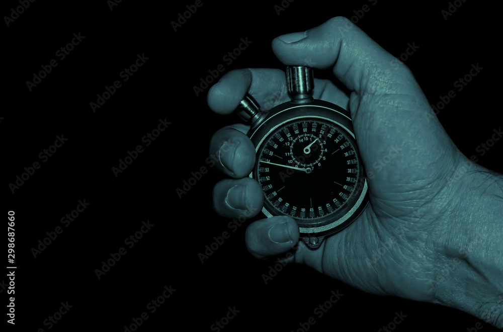 cold blue tone image of hand holding a mechanical stopwatch on black background cold blue tone image of hand holding a mechanical stopwatch on black background