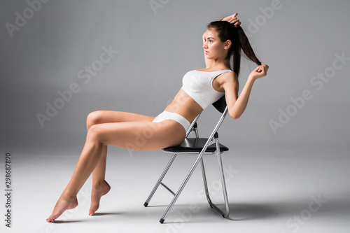 Beautiful woman in white underwear sitting on the chair on grey background.