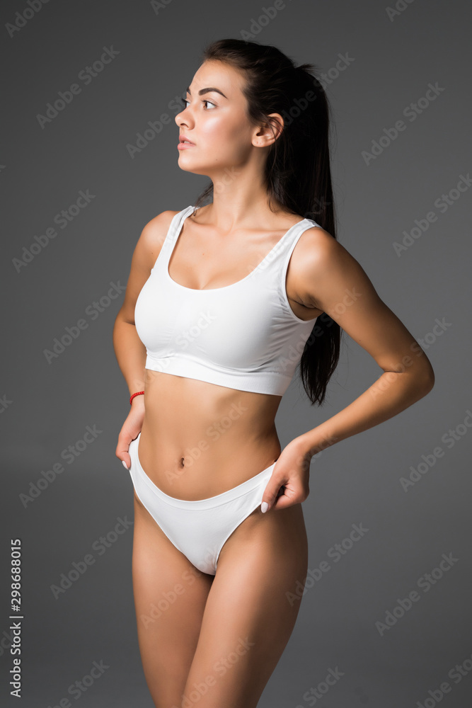 Young beautiful woman body on gray background in white sport clothes Young beautiful woman body on gray background in white sport clothes