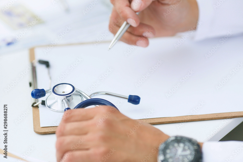 Male doctor on duty in white coat reading patient's information with pen in hand, filling prescription or checklist document close-up. Health and medical concept. Male doctor on duty in white coat reading patient's information with pen in hand, filling prescription or checklist document close-up. Health and medical concept.