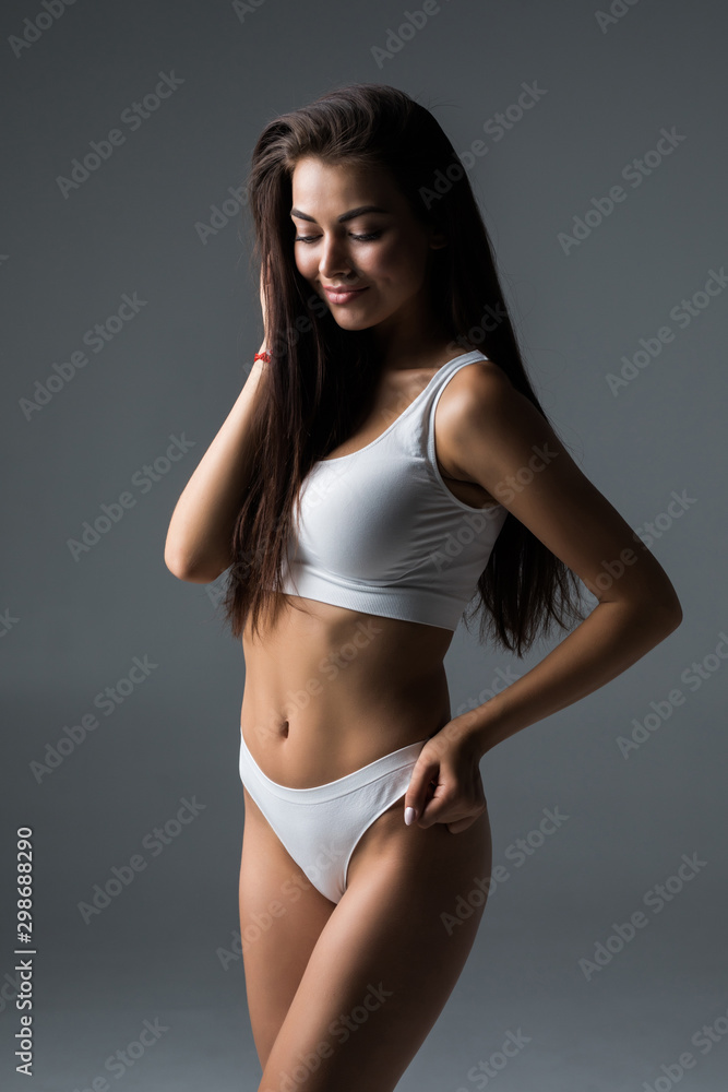 Proud of her perfect body. Attractive young brown hair woman in white lingerie posing against grey background and smiling