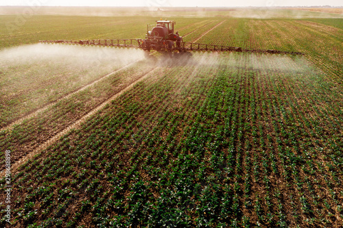 Tractor spraying fertilizer or pesticides on field with sprayer photo