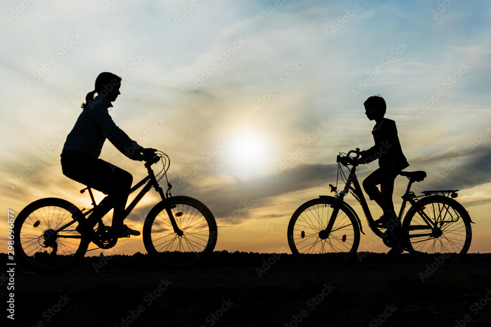 Obraz premium Boy and young girl riding bikes in different directions, silhouettes of riding persons at sunset in nature