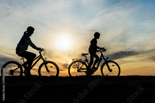Boy and young girl riding bikes in countryside , silhouettes of riding persons at sunset in nature