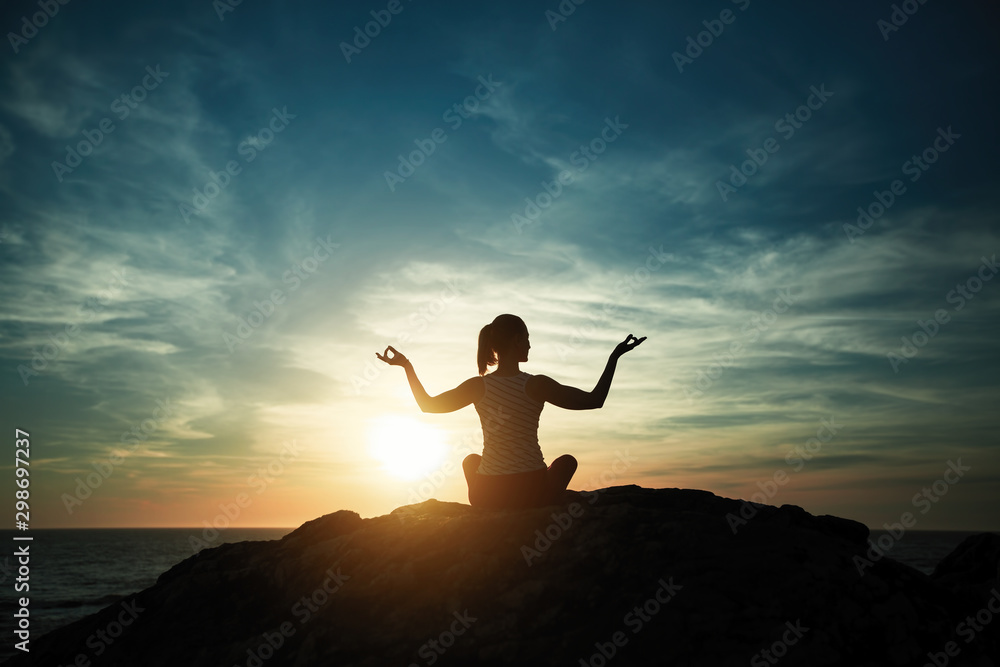 Silhouette of yoga woman sitting in Lotus position on the ocean beach during sunset.