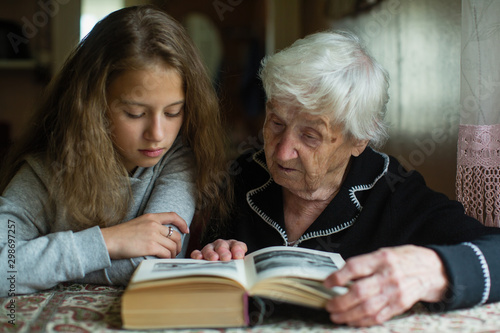 Little cute girl with her old grandma reading a book.
