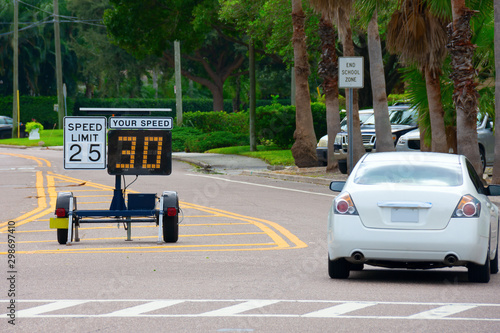 Radar speed limit indicator sign monitored by the police showing 30 miles per hour on the screen proving a passing car is speeding as it drives down the road in a clearly marked school zone.