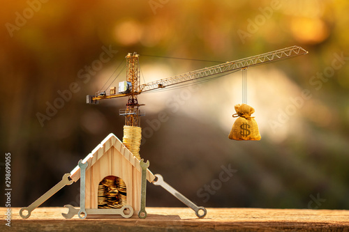 Stack gold coin with increase put on the wooden home and wrench and tower crane with money bag to build new house in garden, saving money and loan for construction real estate concept.